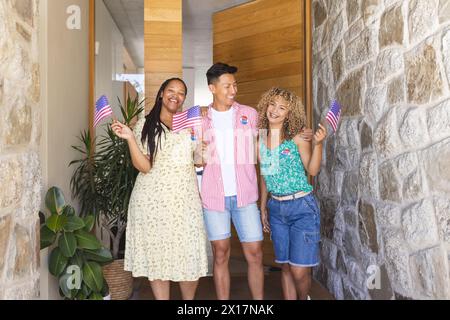 Gruppo di amici, un uomo asiatico e due femmine birazziali, con bandiere americane Foto Stock