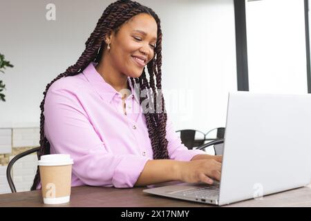 Giovane donna birazziale che indossa una camicia rosa che lavora su un laptop Foto Stock