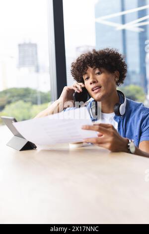 Un giovane uomo birazziale con i capelli ricci sta parlando al telefono in un moderno ufficio d'affari Foto Stock