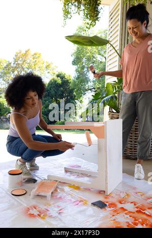 Donna birazziale matura che guarda la giovane donna birazziale dipingere il tavolo a casa per un progetto di upcycling Foto Stock