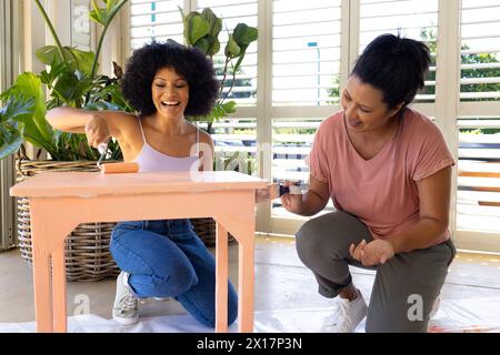 Madre birazziale e figlia adulta dipingono insieme mobili a casa in un progetto di upcycling Foto Stock