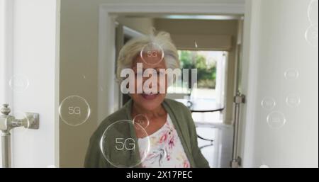 Immagine di un testo di 5g in cerchio su una donna birazziale sorridente che apre la porta di casa Foto Stock