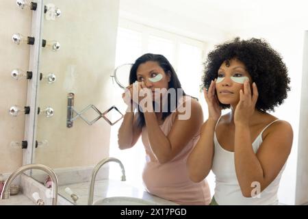 Donna birazziale matura e giovane donna birazziale che applica la cura della pelle a casa in bagno Foto Stock