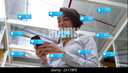 Immagine delle icone dei social media con un numero crescente di persone rispetto a una donna d'affari birazziale che usa lo smartphone Foto Stock