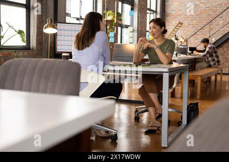 Un team diversificato di professionisti sta discutendo di lavorare alla scrivania in un moderno ufficio aziendale Foto Stock