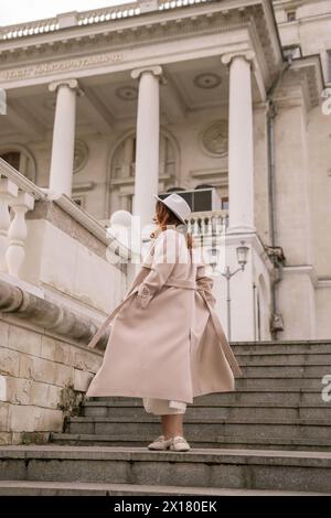 donna con un cappotto e un cappello eleganti su un intricato sfondo architettonico, che fonde armoniosamente la moda moderna con il fascino storico. Il morbido Foto Stock