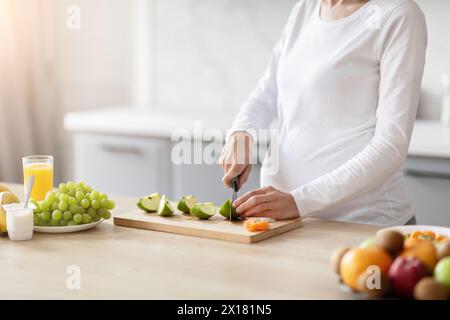 Donna incinta che affetta frutta su un asse di legno Foto Stock