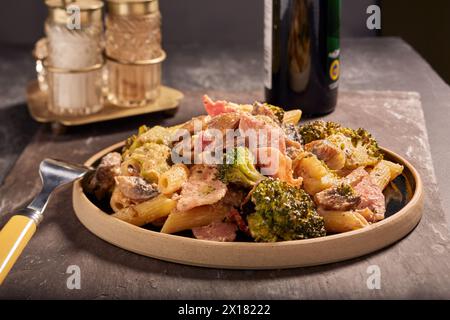 Pasta di pancetta e verdure in una bella salsa cremosa, con alcuni condimenti sullo sfondo. Foto Stock