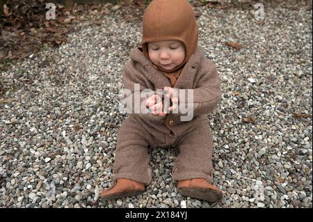 Bambino piccolo, 8 mesi, avvolto caldo, seduto sulla ghiaia e giocando con le pietre, Meclemburgo-Vorpommern, Germania Foto Stock
