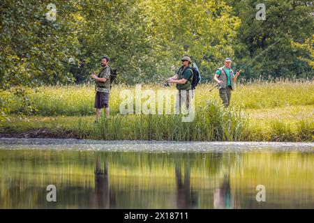 Tre pescatori si divertono a pescare circondati dalla natura lussureggiante della riva del fiume. Hobby e attività all'aperto. Foto Stock