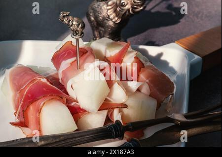 melone con jamon. Tapas spagnole Jamon Iberico con melone e miele su una tavola di legno. Sfondo grigio. Luce dura Foto Stock