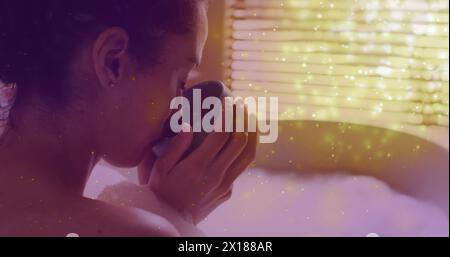 Immagine di macchie di luce sulla donna caucasica che beve caffè e si fa il bagno Foto Stock