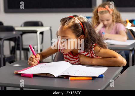 A scuola, giovane studentessa birazziale che si concentra sulla scrittura in classe Foto Stock