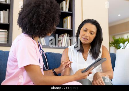 Giovane donna birazziale mostrando tablet a madre matura a casa Foto Stock