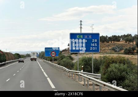 Cartelli autostradali che indicano le distanze e le indicazioni per le città, le auto su strada sotto un cielo nuvoloso, la provincia di Jaen, Andalusia, Spagna Foto Stock