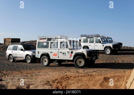 Vicino a Erfoud, diversi veicoli fuoristrada parcheggiati in un paesaggio desertico per un safari, Medio Atlante, Marocco Foto Stock