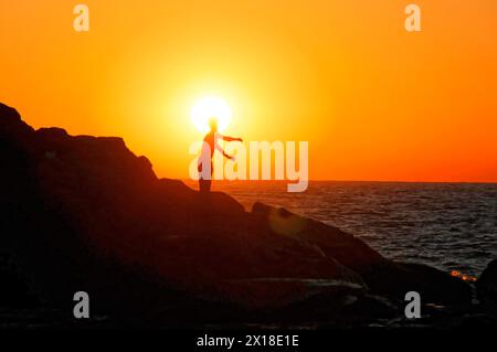 Spiaggia vicino a Poneloya, Las Penitas, Leon, Nicaragua, la persona forma una cornice con le mani di fronte al sole, silhouette sulle rocce al tramonto, Central Foto Stock