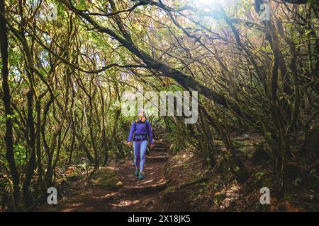 Descrizione: Atletica femminile turistica che percorre sentieri sterrati attraverso una foresta verde in una giornata di sole. 25 Fontes Waterfalls, isola di Madeira, Portuga Foto Stock