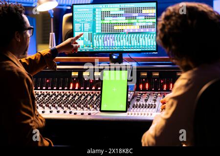 Artista e tecnico del suono che lavora con display greenscreen su tablet, mixando e masterizzando tracce con console audio e software digitale. Musicisti team editing di musica, fader motorizzati. Foto Stock