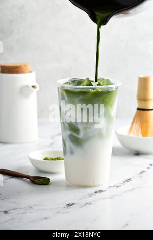 Preparare il latte matcha freddo in un bicchiere alto con ghiaccio aggiungendo tè matcha al latte Foto Stock