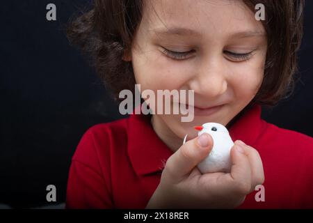 Little Boy tenendo un finto uccello bianco su sfondo scuro Foto Stock