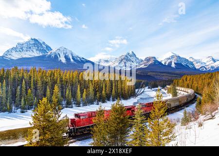 Treno merci rosso che passa attraverso la curva di Morant nella Bow Valley all'interno del Banff National Park. Splendido paesaggio invernale innevato nelle montagne rocciose canadesi di A. Foto Stock