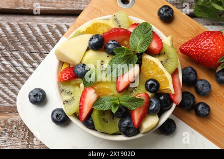 Gustosa Macedonia di frutta nel recipiente e ingredienti su un tavolo di legno, in piano Foto Stock
