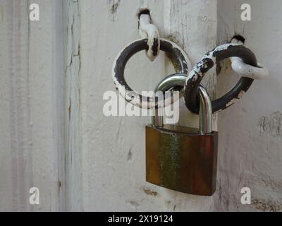 Lucchetto Rusty autentico che tiene chiusa a chiave una vecchia porta d'epoca bianca Foto Stock