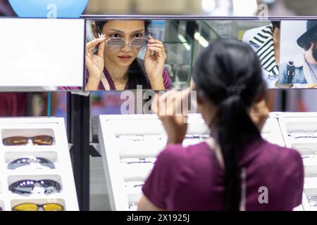 Una giovane donna prova gli occhiali allo specchio in un negozio di ottica Foto Stock