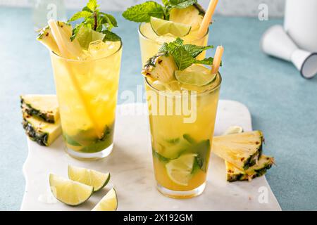 Mojito di ananas con spicchi di menta e lime guarnito con bastoncini di canna da zucchero, foglie di menta e fette di ananas Foto Stock