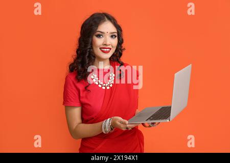 Bella donna indiana in sari con laptop su sfondo arancione Foto Stock