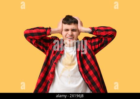 Giovane stressato con macchie di caffè sulla sua t-shirt su sfondo arancione Foto Stock