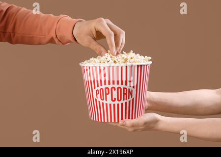 Mano maschio che prende popcorn dalla benna mani femminili che tengono su sfondo marrone Foto Stock