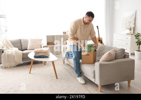 Giovane uomo che confeziona vestiti piegati in scatola sul divano di casa Foto Stock