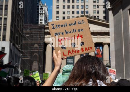 New York, Stati Uniti. 15 aprile 2024. Un manifestante ha un cartello che dice: "Israele e gli Stati Uniti stanno costruendo sul genocidio", il gruppo di attivisti pro-palestinesi durante la nostra vita ha organizzato una protesta all'11 di Wall Street. La protesta in seguito tentò di marciare attraverso il ponte di Brooklyn come parte di un tentativo multi-città/multi-paese di creare un "blocco economico" in solidarietà con la Palestina. Sono stati fatti diversi arresti. (Foto di Syndi Pilar/SOPA Image/Sipa USA) credito: SIPA USA/Alamy Live News Foto Stock