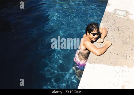 Adolescente asiatico appoggiato sul bordo piscina fuori a casa, godendosi il sole, copiando spazio Foto Stock