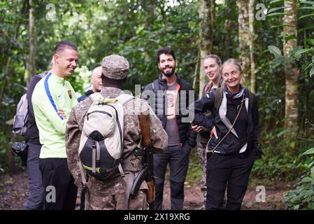 Nel mezzo della lussureggiante vegetazione del Parco Nazionale di Kibale, i turisti che indossano un abbigliamento da safari si impegnano in un briefing informativo condotto dalla loro guida armata, preparandosi Foto Stock