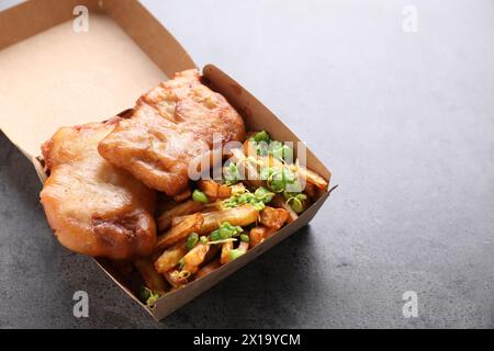 Gustoso pesce, patatine e piselli in scatola di carta sul tavolo grigio, primo piano. Spazio per il testo Foto Stock