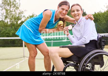 Un momento di gioia in cui una donna su una sedia a rotelle e un altro atleta in piedi mostrano insieme una medaglia d'oro, simboleggiando la vittoria e l'inclusione nel tennis Foto Stock