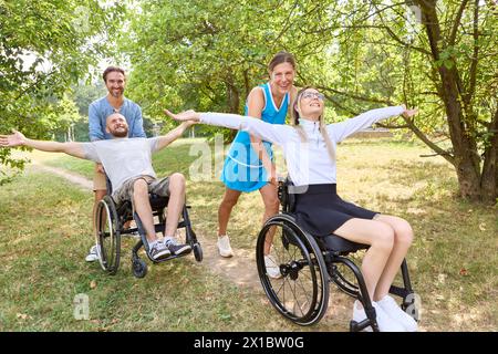 Un gruppo di amici, tra cui due persone su sedia a rotelle, si godranno un momento felice all'aperto, mostrando diversità e accessibilità in un parco soleggiato. Foto Stock