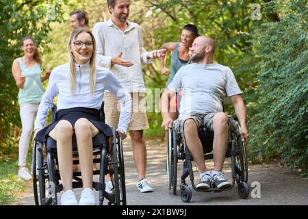 Un gruppo eterogeneo di persone, comprese persone su sedia a rotelle, trascorrono felicemente del tempo insieme in un parco. Foto Stock