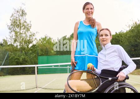 Due persone che trascorrono del tempo su un campo da tennis; una in piedi e una in sedia a rotelle, mostrando l'inclusione e lo stile di vita attivo. Foto Stock