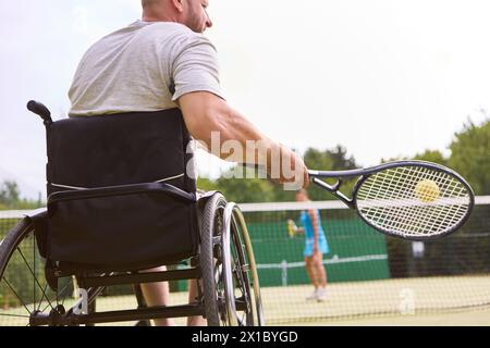 Una persona attiva che utilizza una sedia a rotelle per partecipare a una partita di tennis all'aperto, dimostrando l'inclusione e la determinazione. Foto Stock