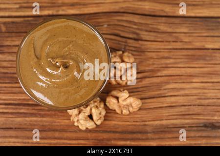 Delizioso burro di noci nel recipiente e noci sul tavolo di legno, vista dall'alto. Spazio per il testo Foto Stock