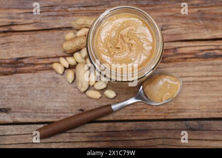 Gustosa pasta di arachidi in vaso e cucchiaio su un tavolo di legno, stendere in piano Foto Stock