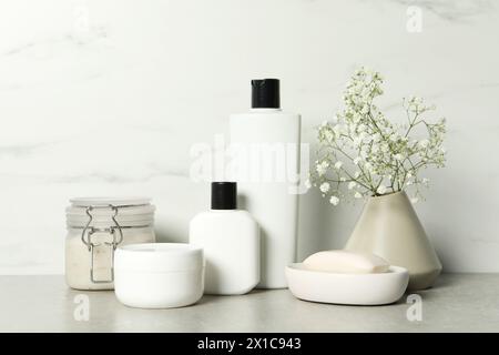 Accessori per il bagno. Prodotti per la cura della persona e fiori di gypsophila in vaso su tavolo grigio vicino alle pareti in marmo bianco Foto Stock