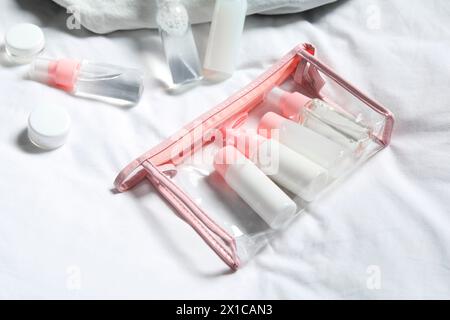 Kit da viaggio cosmetico. Sacchetto di plastica con piccoli contenitori di prodotti per la cura personale sul letto Foto Stock