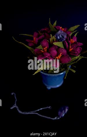 un anello di ametista e un ciondolo di fiori di carta in un vaso blu su sfondo nero Foto Stock