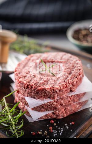 Polpette di manzo crude fresche con sale al rosmarino e pepe preparate in forma di carne su un tagliere. Foto Stock