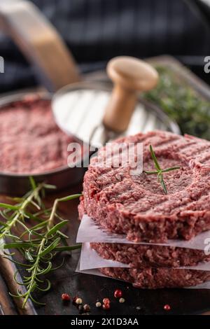 Polpette di manzo crude fresche con sale al rosmarino e pepe preparate in forma di carne su un tagliere. Foto Stock